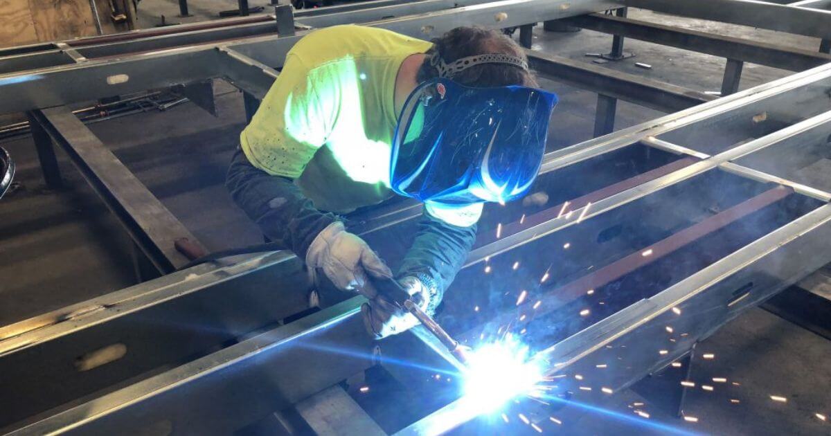 Prefabrication process welding done on large steel beams by prefab construction company employee